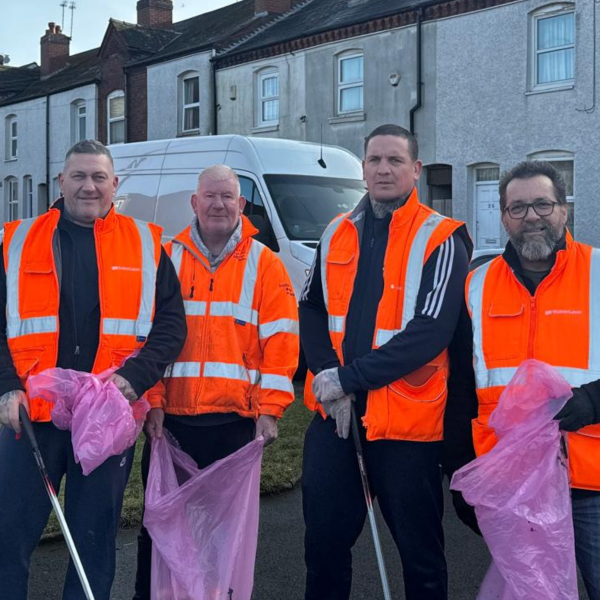 four men wearing orange hi-vis vests smiling at the camera holding purple bin bags litter picking