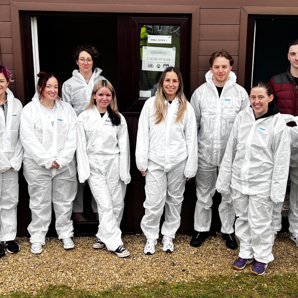 10 individuals wearing white all-in-ones, facing front towards the camera smiling